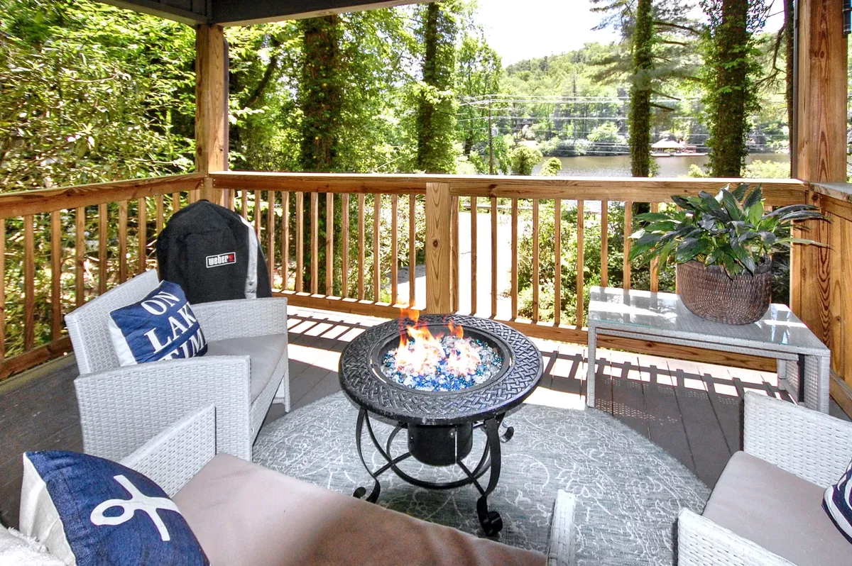 This inviting exterior scene features a cozy fire pit surrounded by comfortable outdoor seating, lush greenery, and a stunning lake view in the background. The setting is ideal for relaxing, entertaining, or simply enjoying the tranquil outdoors, perfectly capturing the essence of gathering around the fire in a picturesque natural setting.