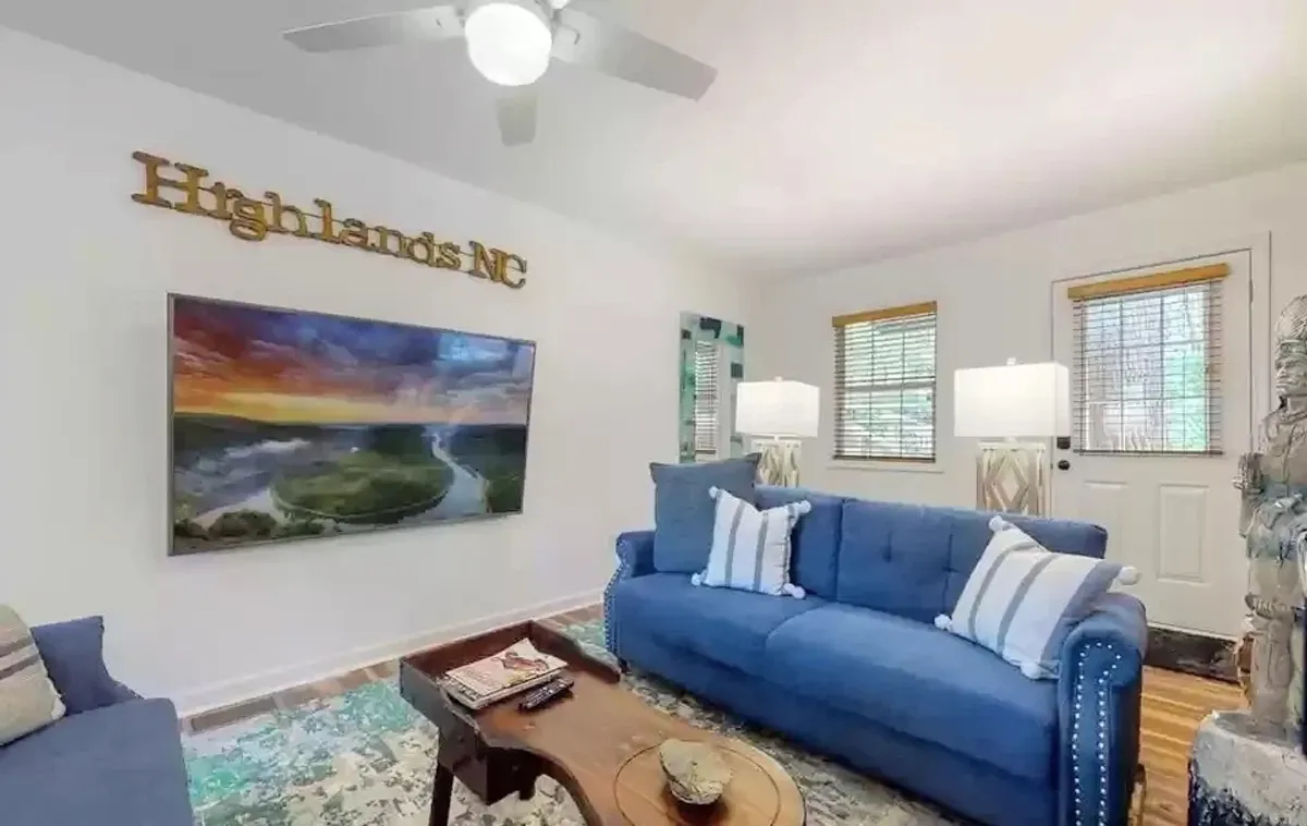 A welcoming living space featuring a plush blue couch, vibrant artwork, a wooden coffee table, and soft lighting from the lamps. The arrangement suggests a cozy spot for relaxing, socializing, or enjoying entertainment like TV or board games.