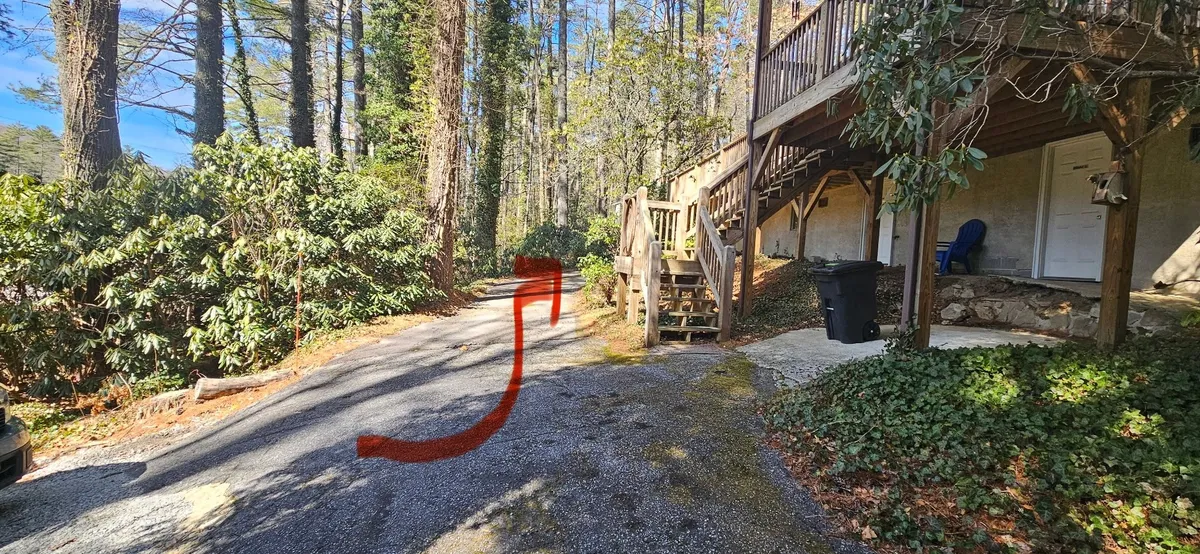 An exterior closer view of the property, showing the gravel driveway, wooden stairs, and lush greenery that invites exploration. The image hints at the welcoming front porch and the possibility of enjoying coffee outside or discovering the natural surroundings.