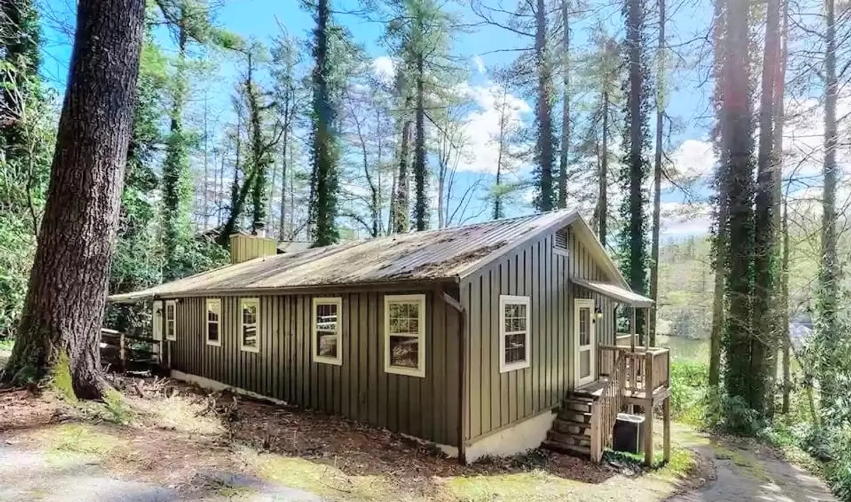 The rustic wooden cabin stands amid a lush forest, with a front porch that beckons for morning coffee or quiet moments after a day on the trails. The scene is peaceful, highlighting both the shelter and the surrounding wilderness.