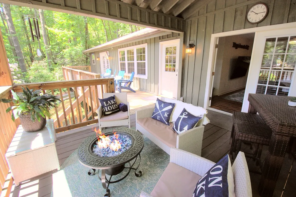 A cozy outdoor seating area encircling a fire pit, with decorative pillows and abundant greenery in the background. The scene exudes comfort and is ideal for gatherings, storytelling, and relaxing after a day at the lake.