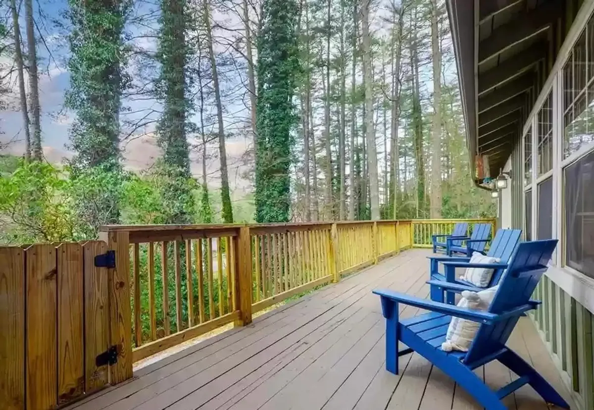 A spacious wooden deck with blue chairs surrounded by trees, offering a peaceful retreat for relaxation, reading, or enjoying morning coffee outdoors.