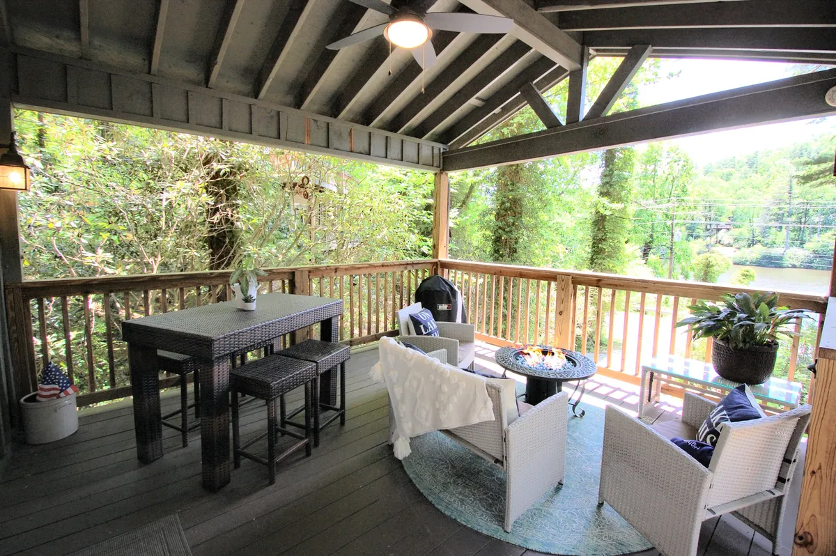 A welcoming outdoor dining area on a deck, featuring a table and comfortable seating surrounded by lush greenery. The fire pit is ready for evening gatherings, and the space offers views of the sunset and sunrise, making it ideal for family relaxation and socializing.