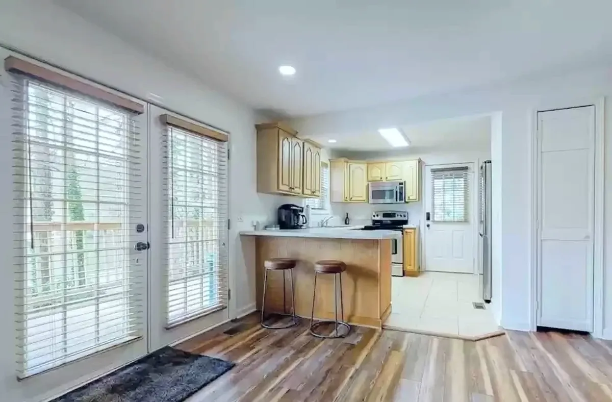A bright, welcoming kitchen interior with a central island, stools, and large windows that let in natural light. The space feels perfect for group gatherings, morning coffee rituals, or cozy indoor activities during cooler seasons.